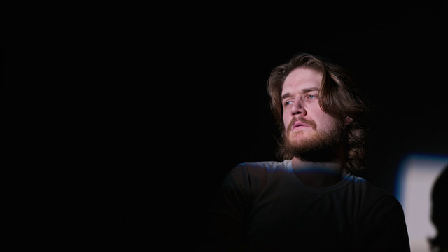 a man with long hair standing in the dark