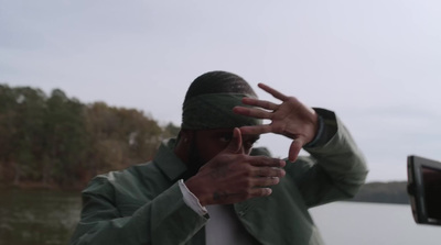 a man in a green jacket holding his hands up to his face