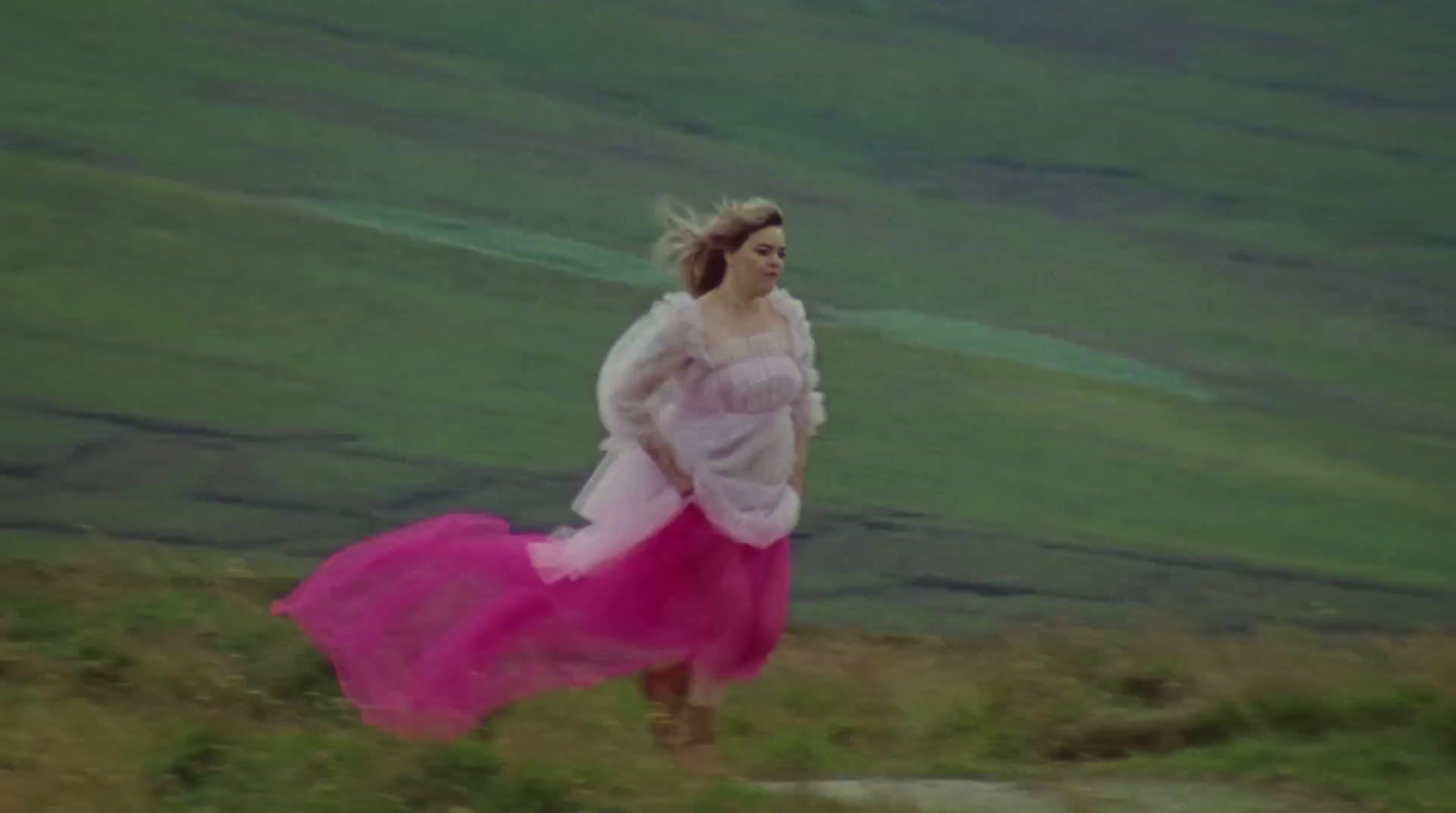 a woman in a pink dress is walking on a hill