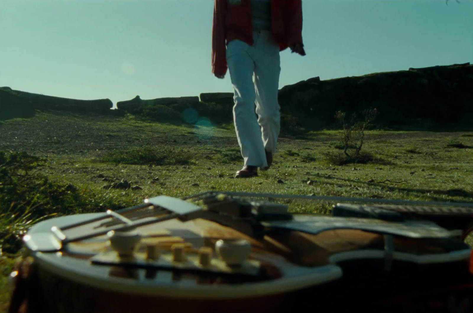 a man walking across a field next to a guitar