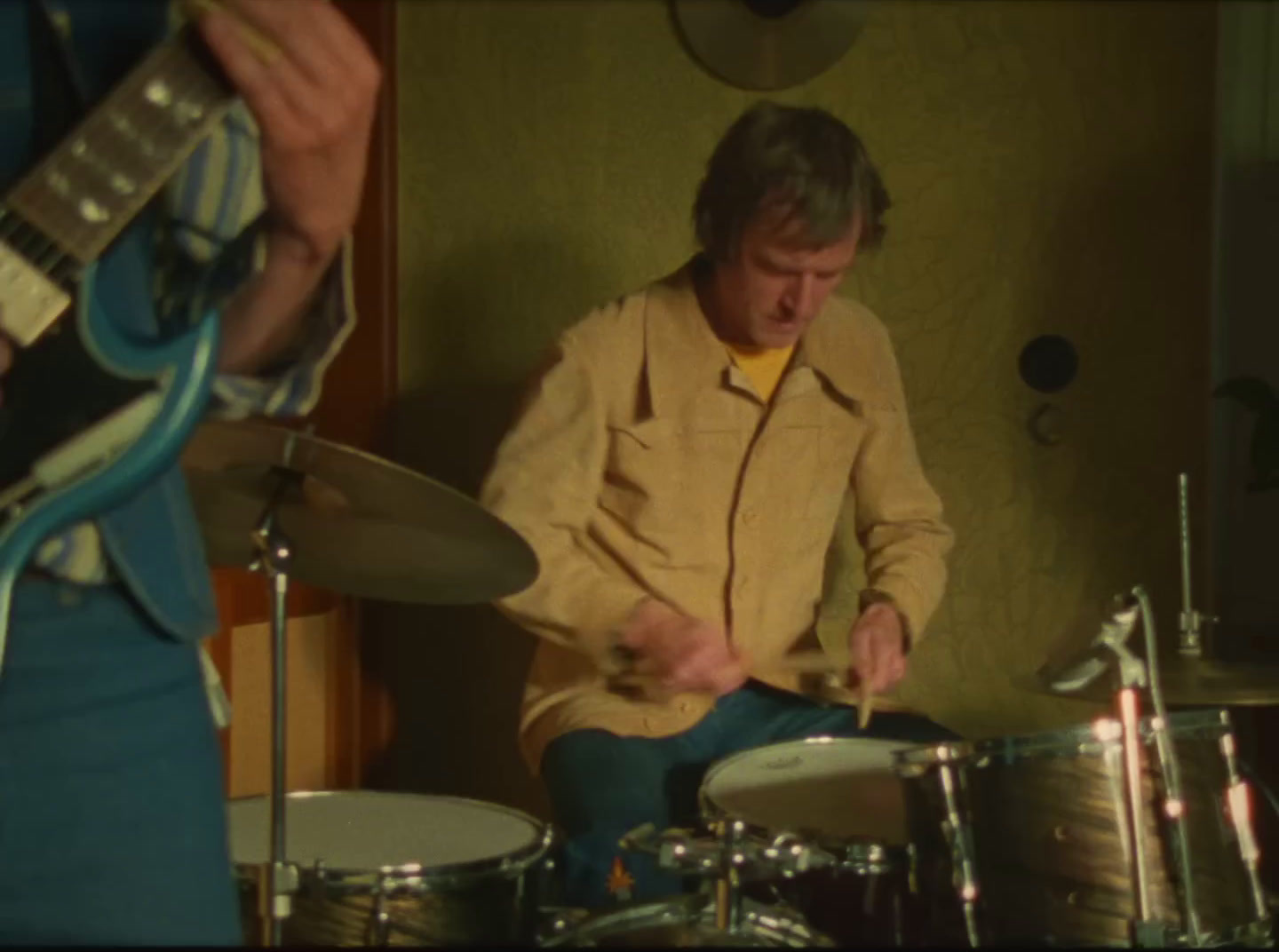 a man playing drums while another man plays a guitar