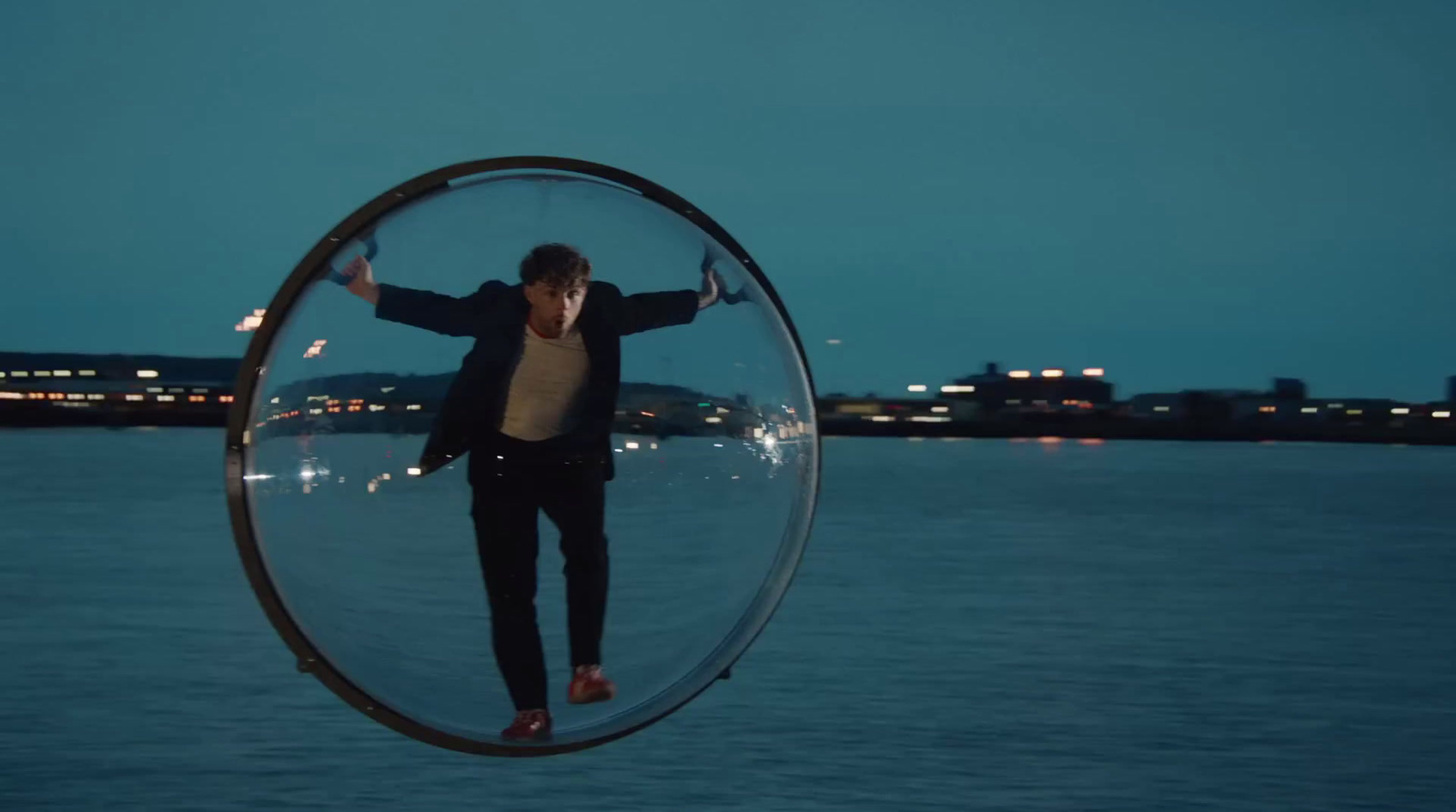 a man standing inside of a glass ball on top of a body of water