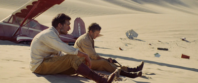 two men sitting in the sand near a plane