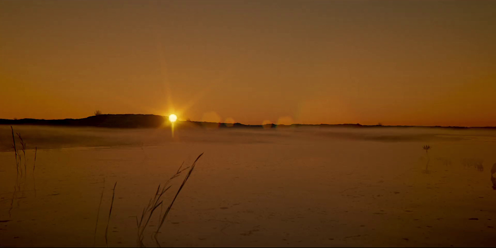 the sun is setting over a snowy field