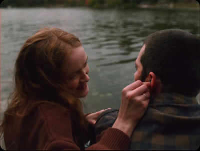 a man holding a woman's ear next to a body of water