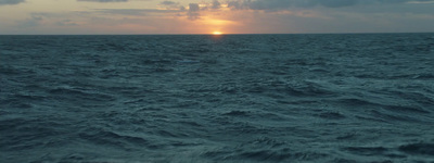 a large body of water with a sun setting in the distance