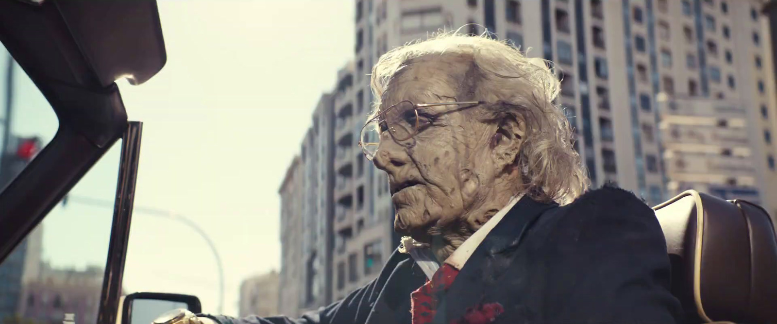 an old man in a suit and tie driving a car