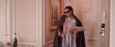 a woman in a coat and sunglasses is standing in a hallway