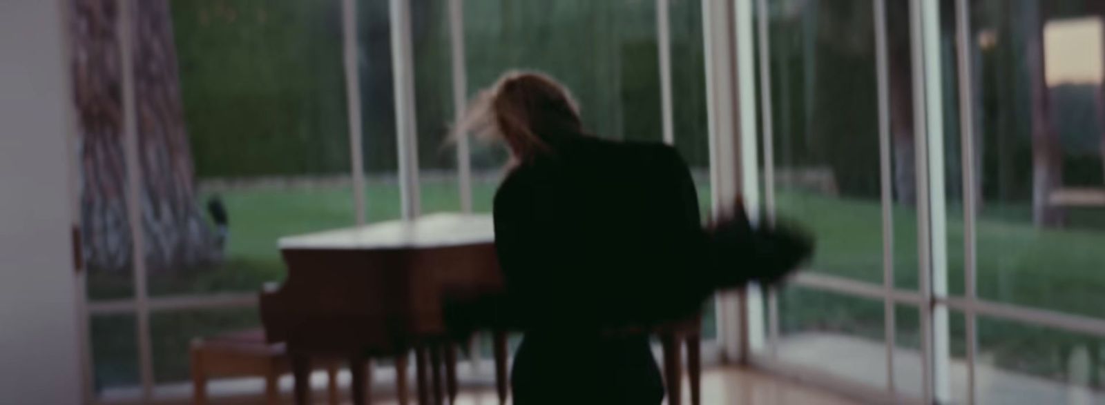 a woman standing in front of a window next to a piano