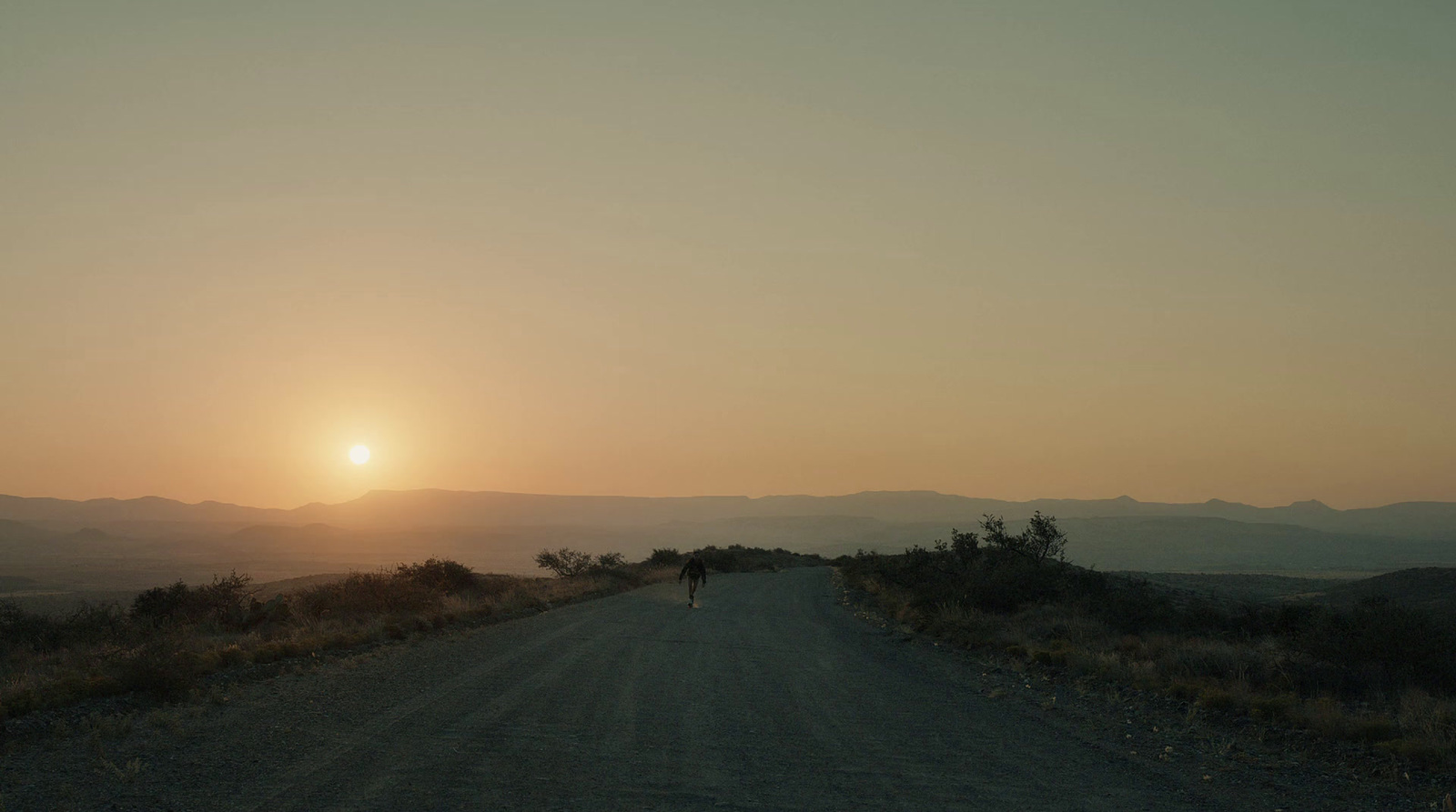 a person walking down a dirt road at sunset