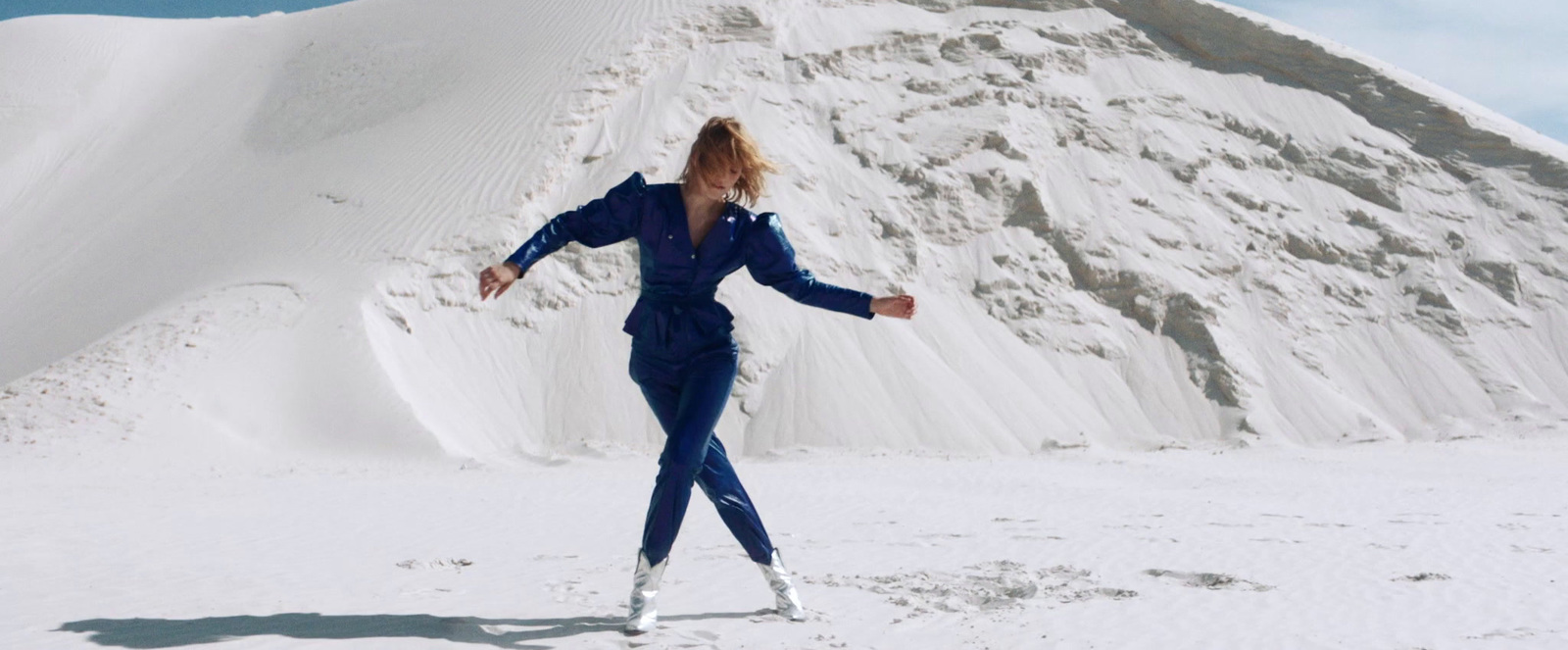 a woman in a blue jumpsuit standing in front of a mountain