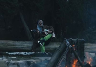 a woman sitting on a log playing a guitar