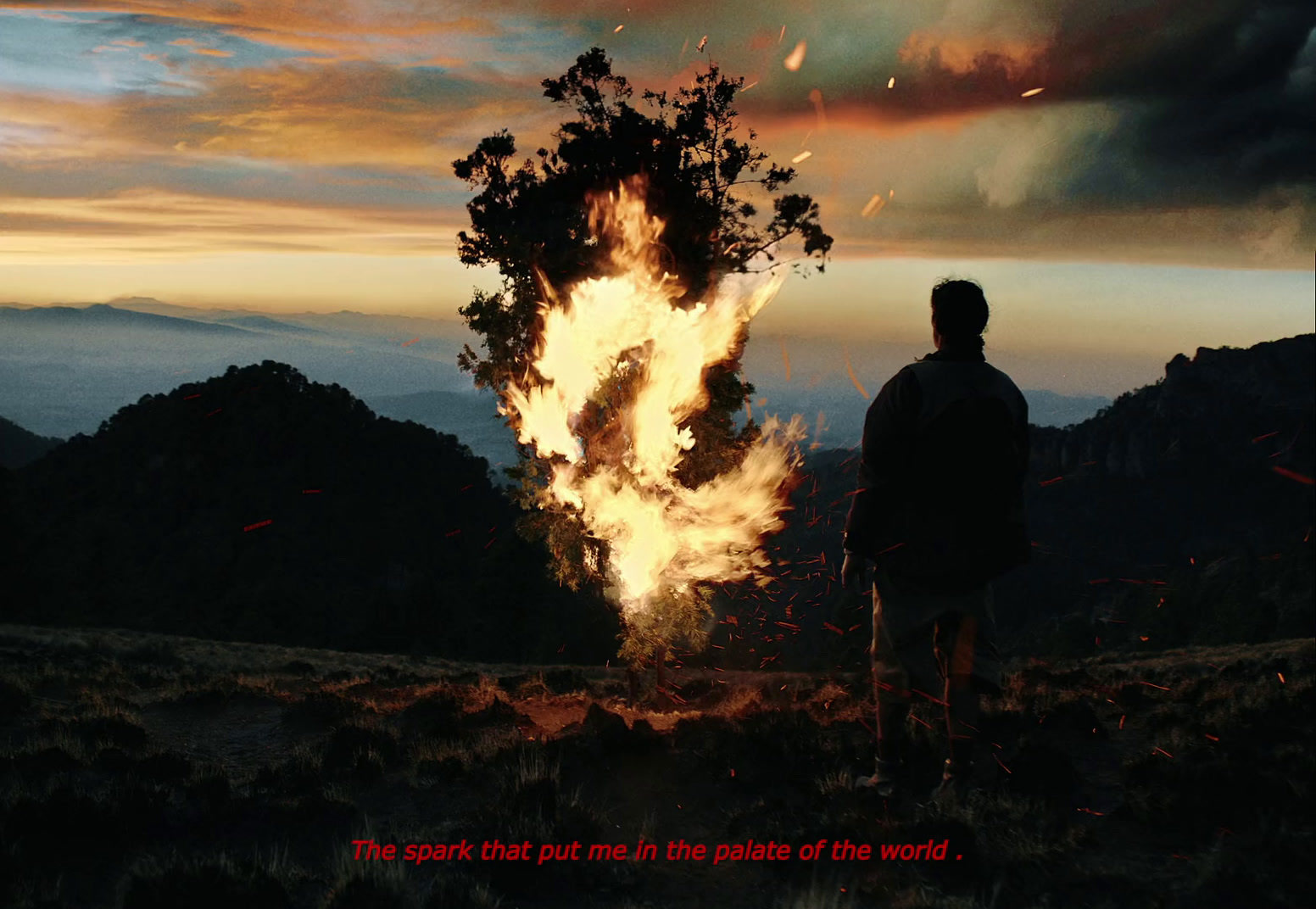 a man standing in front of a fire on top of a hill