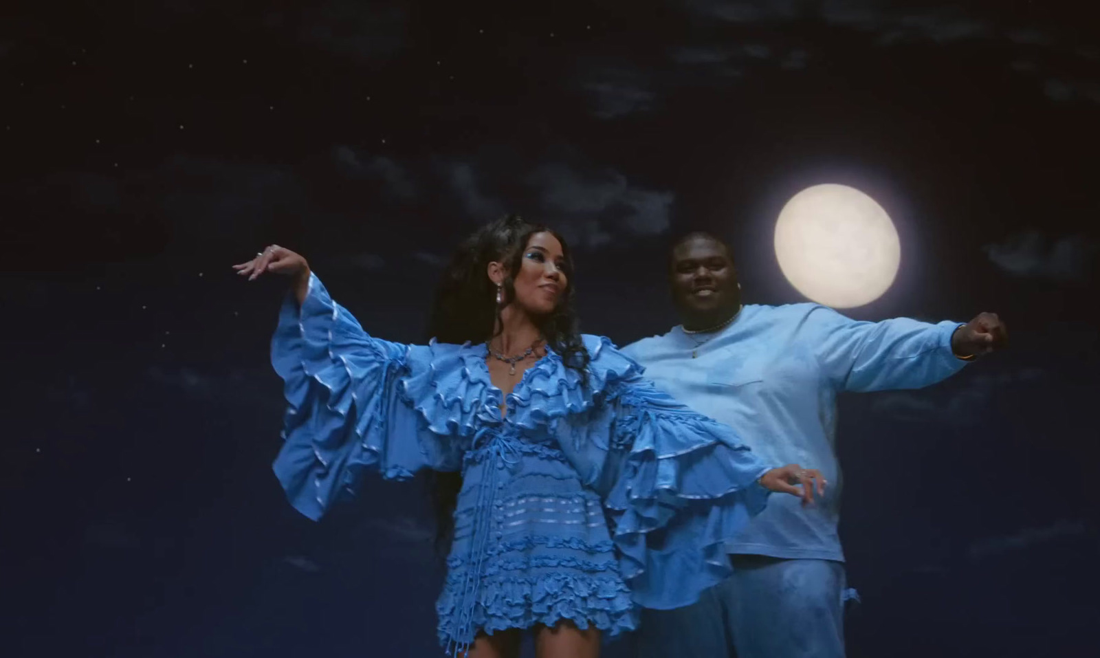 a man and a woman standing in front of a full moon