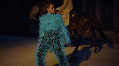 a woman in a blue feathered outfit walking a horse