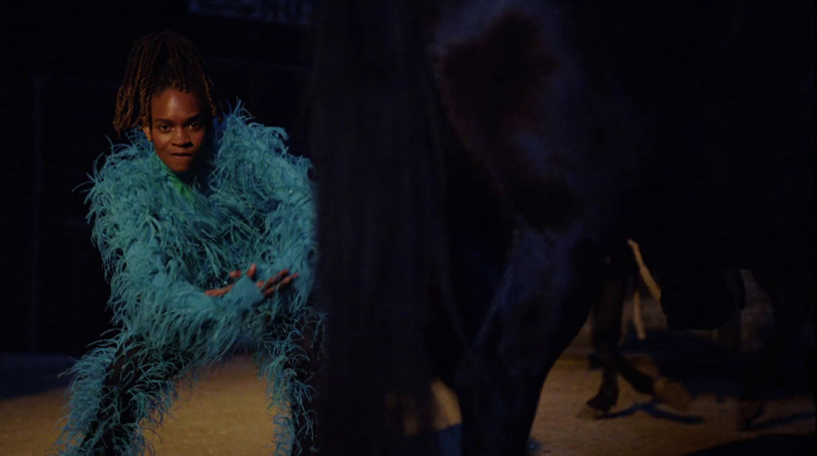 a man in a blue feather coat standing next to a black horse