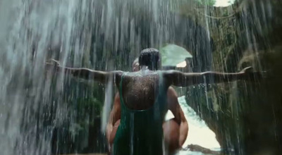 a woman in a green bathing suit sitting under a waterfall