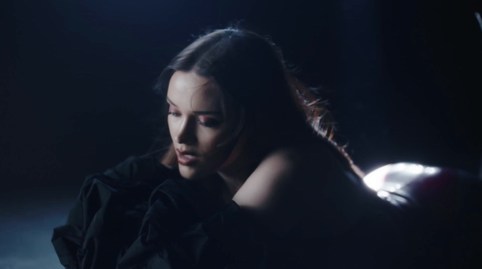 a woman sitting in the dark with her hand on her shoulder