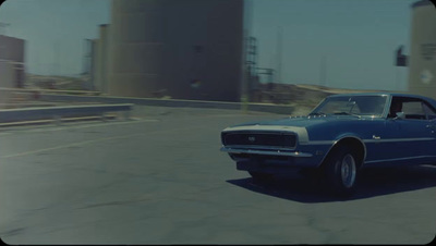 a blue car driving down a street next to tall buildings