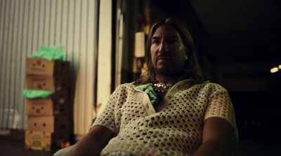 a man with long hair wearing a sweater and a necklace