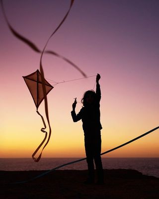 a woman is flying a kite on the beach