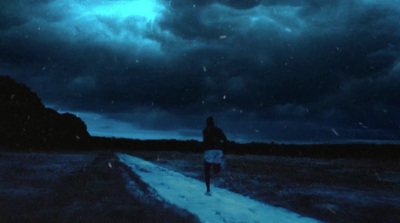 a man walking down a road under a cloudy sky