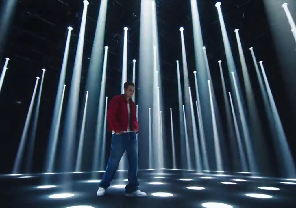 a man in a red jacket standing in front of a row of white lights