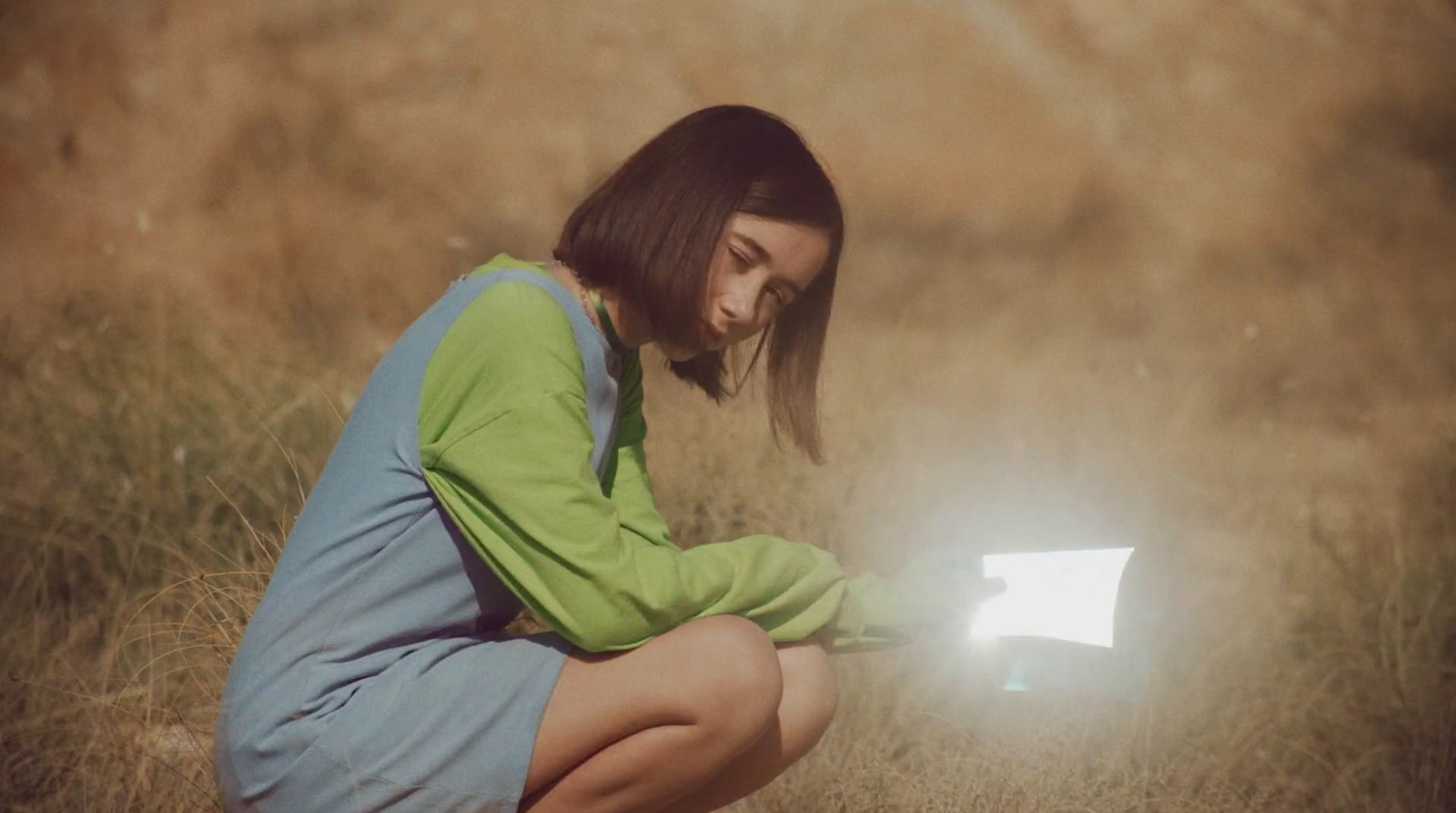 a woman kneeling down in a field with a laptop