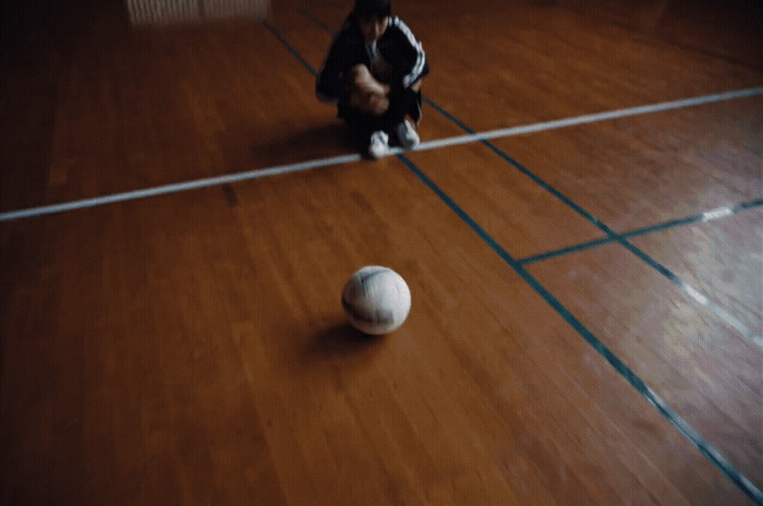 a person kneeling down next to a ball on a hard wood floor