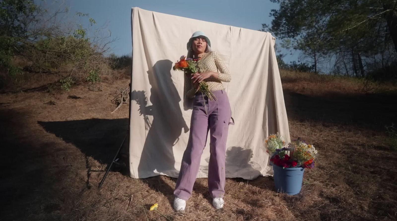 a woman standing in front of a white sheet holding flowers