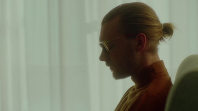 a man with a ponytail and glasses looking out a window