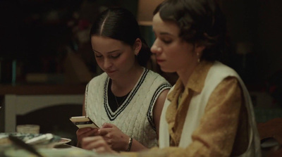 two women sitting at a table looking at a cell phone