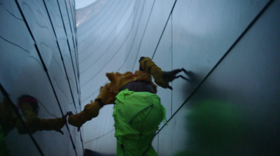 a man in a green jacket climbing up the side of a building