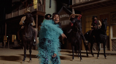 a woman in a blue feather dress standing in front of a group of horses