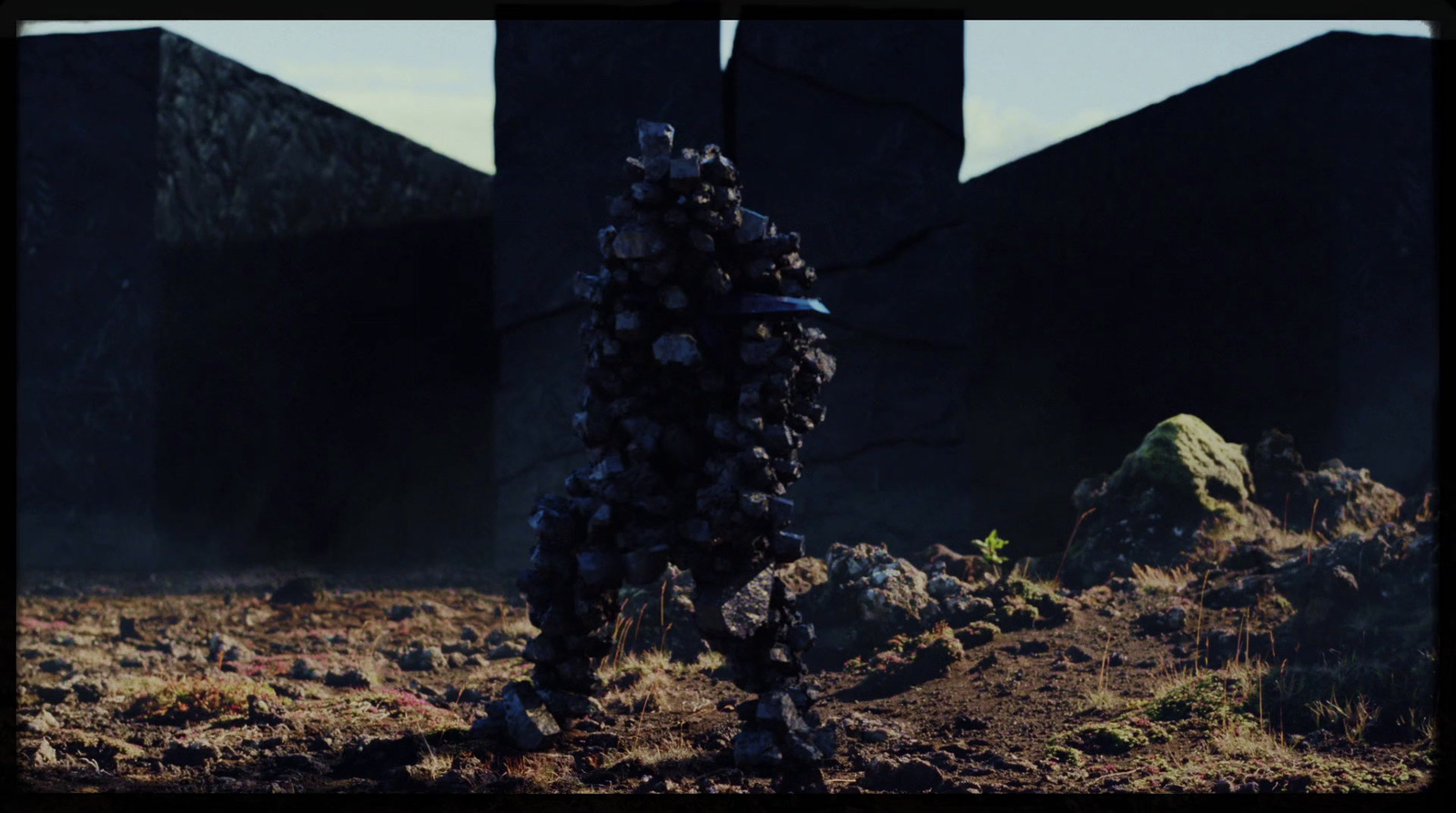 a man standing in a field next to a pile of rocks