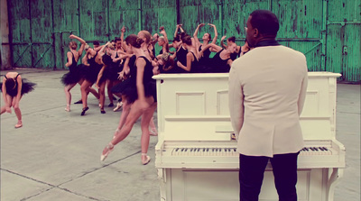 a man standing in front of a piano with dancers behind him