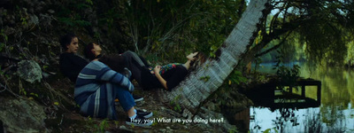 two people sitting in a hammock next to a body of water