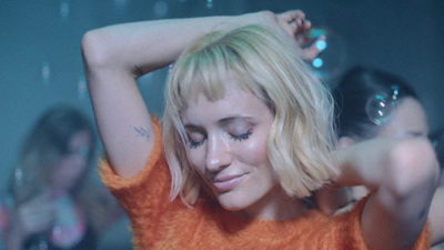 a woman in an orange sweater holding her hair in the air