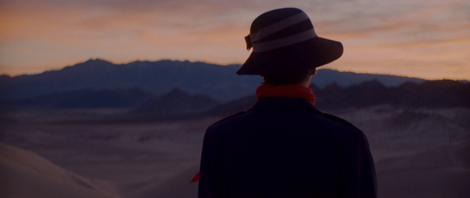 a man wearing a hat standing in front of a mountain