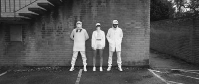 a group of three people standing next to a brick wall