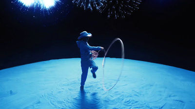 a man in a suit and hat juggling a hoop with fireworks in the background