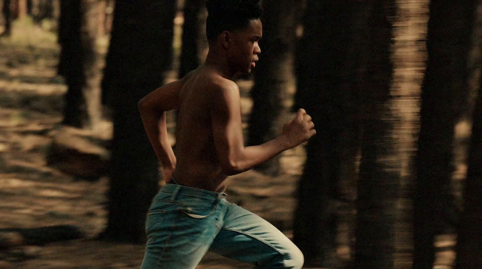 a shirtless man running through a forest