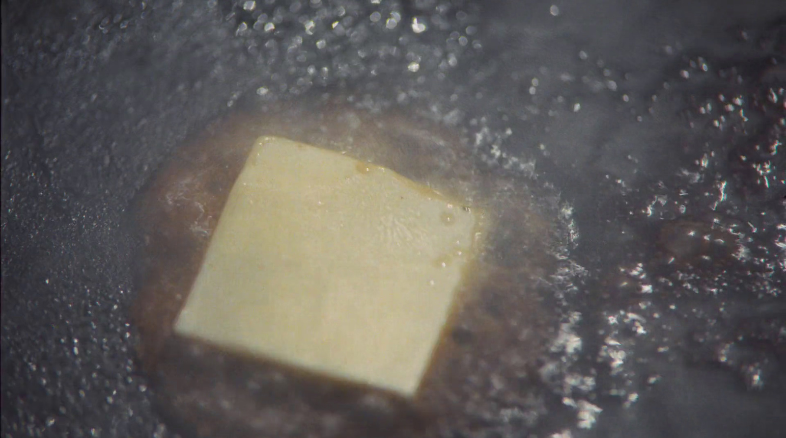 a square of butter cooking in a frying pan