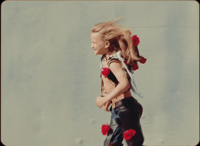 a little girl walking down a street with flowers in her hair