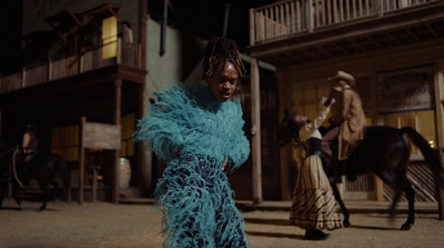 a woman in a blue feathered dress standing in front of a horse