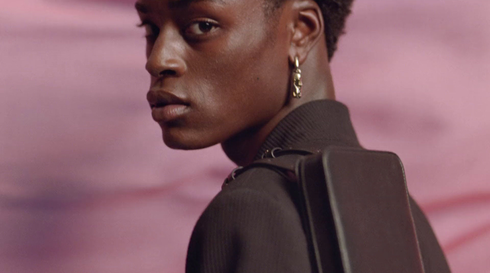 a woman in a brown jacket and gold earrings