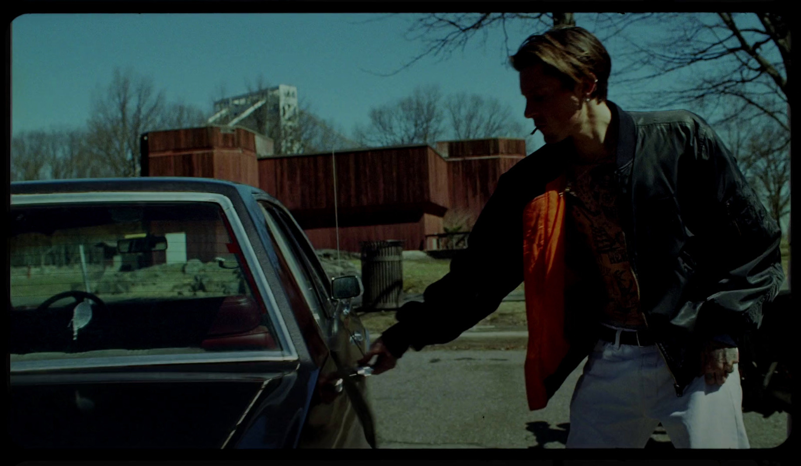 a man in a black jacket and a red tie standing next to a car