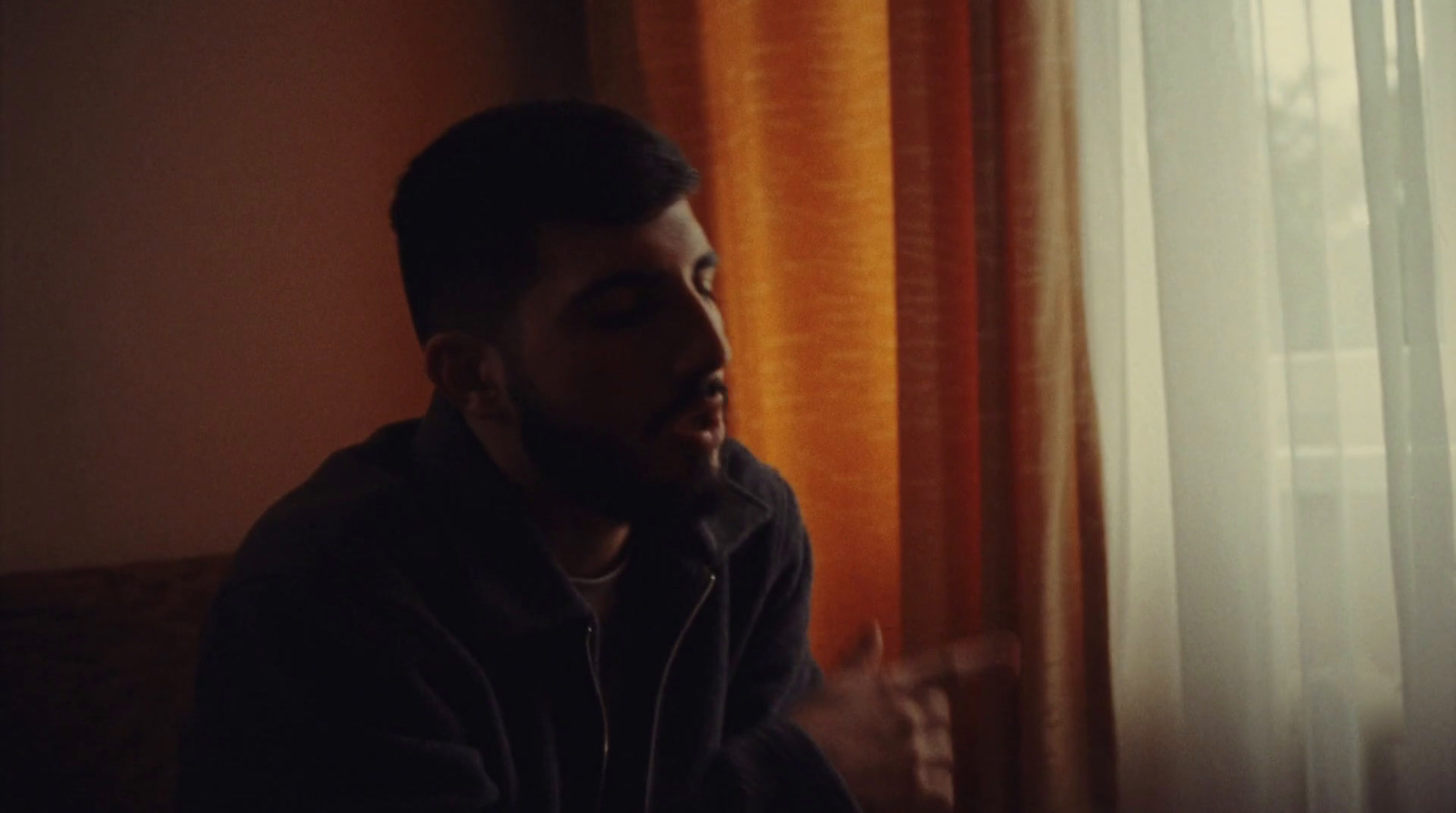 a man sitting in front of a window next to a curtain