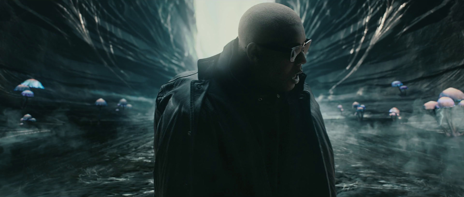 a man in a black jacket and glasses standing in a dark tunnel