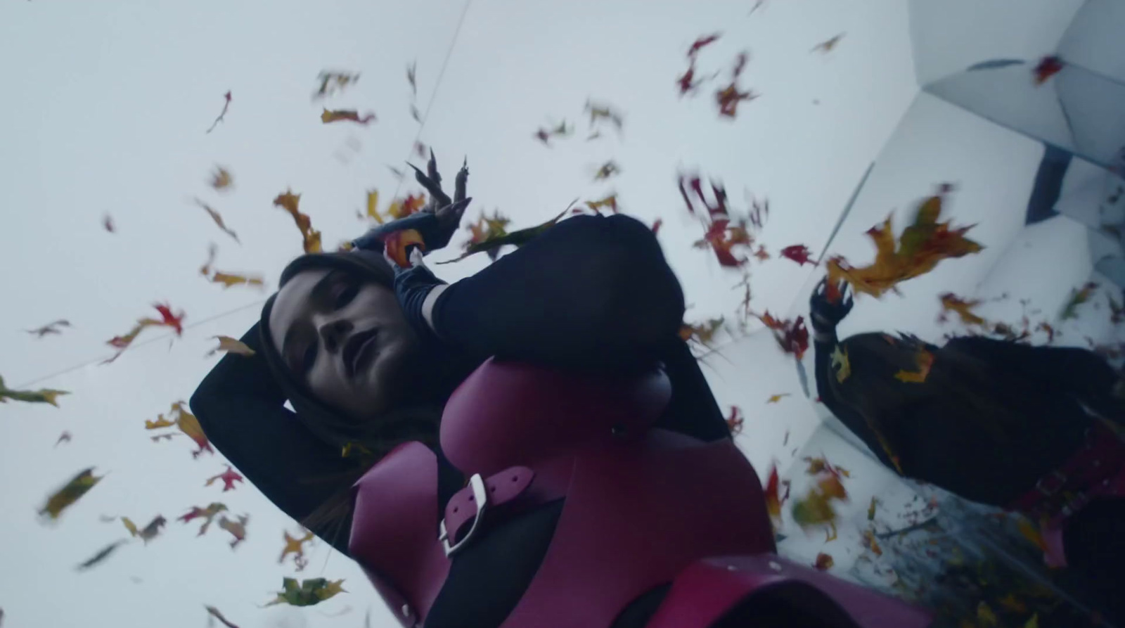 a woman in a pink and black suit is surrounded by leaves